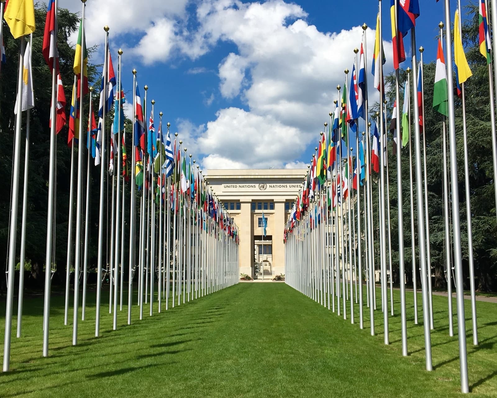 Two rows of national flags leading to the United Nations Palais des Nations in Geneva under a blue sky